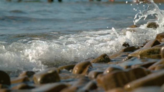 特写: 小泡沫海浪席卷棕色卵石滩。