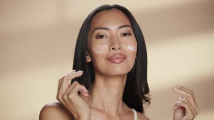 女性美女肖像。美丽的亚洲黑发女人触摸自然，健康的皮肤，使用面部保湿霜，涂抹面霜。孤立背景下的健康和护