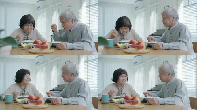 迷人的年轻亚洲老年人夫妇快乐地坐着聊天，在老年人的日常生活方式中，早上在家里的餐桌上吃健康营养早餐的