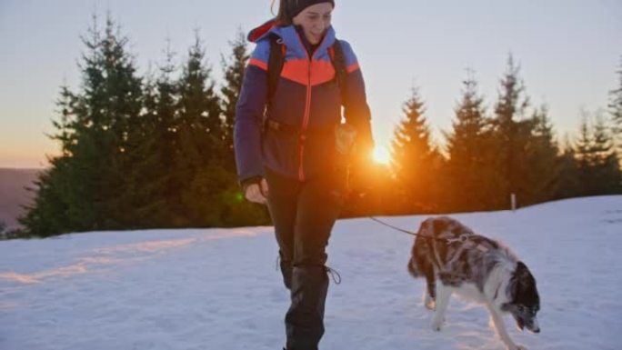 日出时，SLO MO女人带着她的狗在雪坡上散步