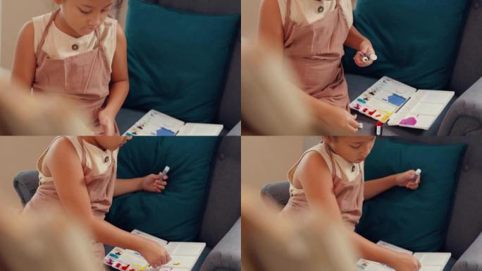 特写亚洲学步女孩围裙坐在油画画布前的沙发椅把丙烯酸色放在调色板上在家客厅使用调色板刀混合颜色。