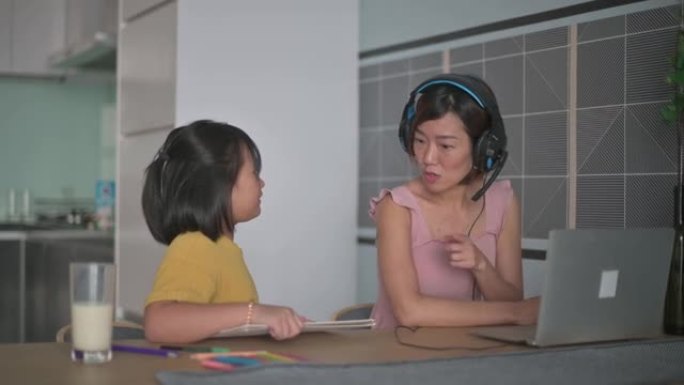 亚洲华裔女商人在家与同事进行视频通话，而女儿在餐桌上做作业