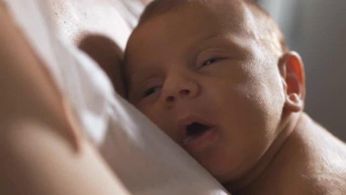 新生婴儿的脸在母亲的怀抱中平静地睡着的真实特写。小宝宝在被父母摇晃入睡时做了快乐的梦。新生活和为人父