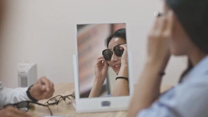 亚洲中国美女试戴墨镜照镜子在眼镜店微笑