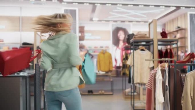 服装店: 柜台上的年轻女子从友好的零售助理那里拿起带有衣服的购物袋，心情愉快，微笑，旋转和跳舞。拥有