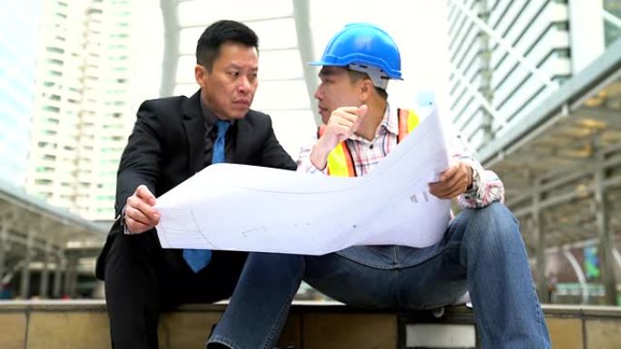 商人和工程师正在使用纸质蓝图讨论该项目。作为高层建筑大城市场景背景下的交流工具