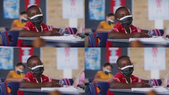 戴着口罩，坐在教室里看着相机的非裔美国小学生的肖像