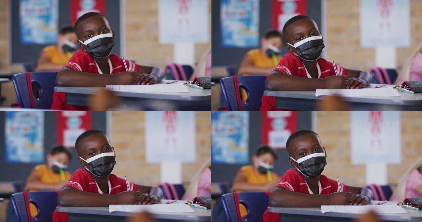 戴着口罩，坐在教室里看着相机的非裔美国小学生的肖像