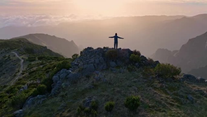 人站在山顶上，看着日出的天空。马德拉岛山区壮丽日出的鸟瞰图。山里的登山者实现了他的目标，享受着美妙的