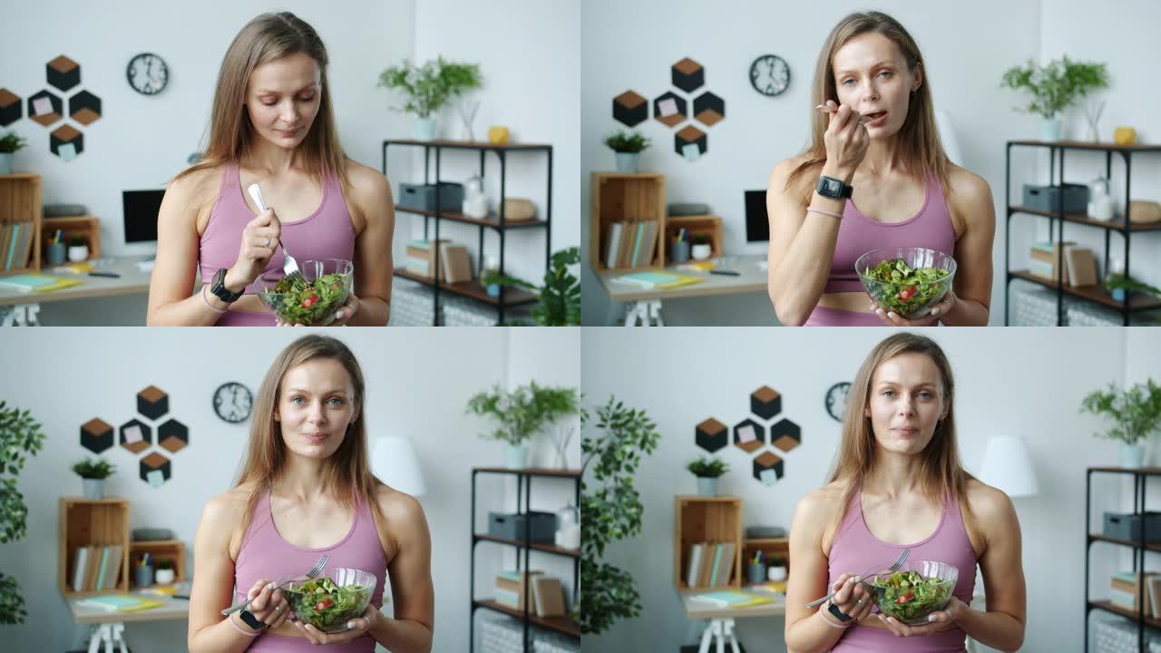 美丽的年轻女士吃蔬菜沙拉和微笑站在家里的慢动作肖像