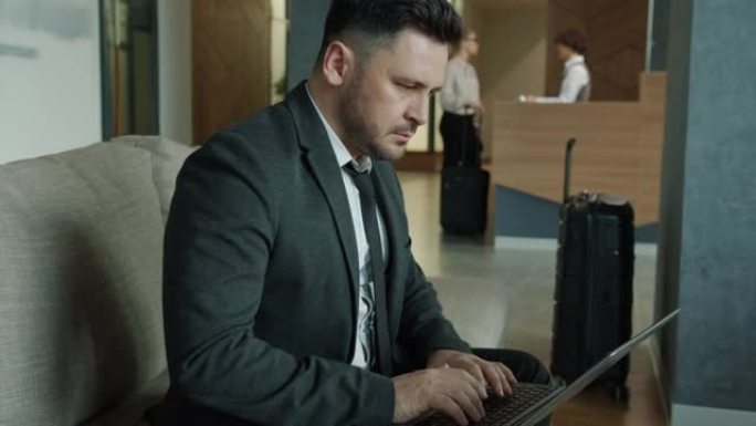 女客人在背景中登记入住时，商人使用笔记本电脑在酒店大堂工作
