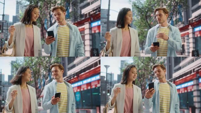 年轻时尚的多民族夫妇在大城市的街道上随意行走。英俊的白人男性向美丽的日本女性展示智能手机。不同的朋友