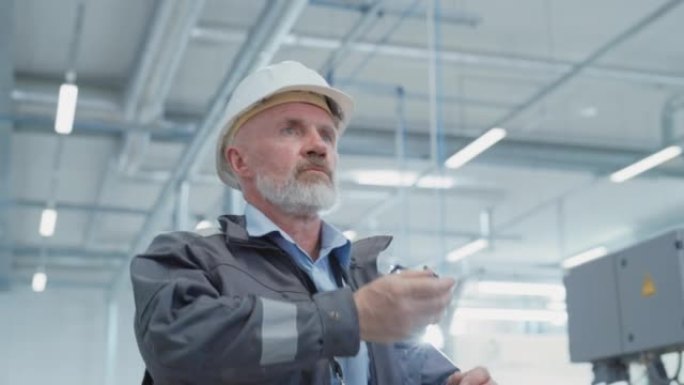 一位中年成功的男性工程师在电子制造工厂散步时戴上白色安全帽和安全眼镜的肖像。重工业专家摆姿势拍照。