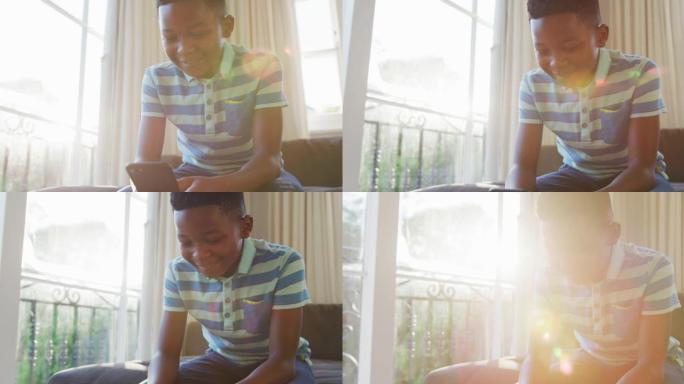 快乐的非洲裔美国男孩坐在沙发上，用智能手机微笑，被阳光照射