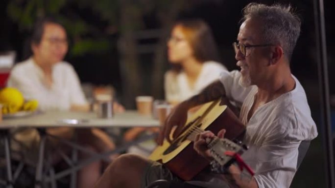 喜欢弹吉他的亚洲华裔老人家人和朋友喜欢玩乐器花园派对聚会露营帐篷晚上