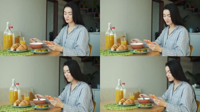 亚洲妇女在家里的厨房里吃早餐和使用智能手机的肖像