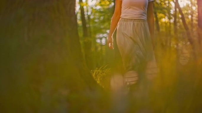 穿着白色长裙的SLO MO女人赤脚在高高的草丛中行走时碰到树木