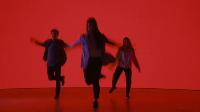 由三位时尚的专业舞者组成的多元化小组，在工作室环境中的虚拟制作过程中，在带有红色背景的大Led墙屏幕