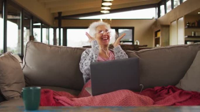 坐在沙发上的高级混血妇女使用笔记本电脑进行视频通话