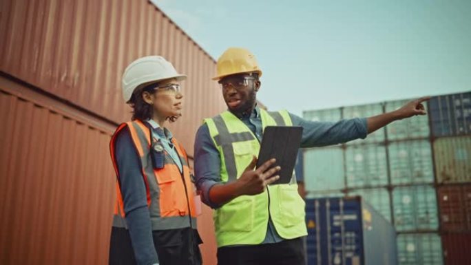 多民族女性工业工程师，平板电脑和黑人非洲裔美国男性主管，戴着安全帽和安全背心站在集装箱码头。同事们谈