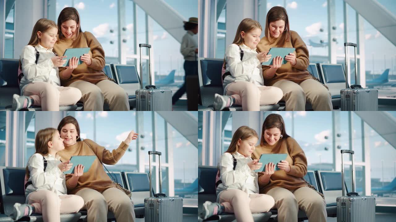 机场航站楼: 可爱的母亲和小女儿等待他们的假期航班，在数字平板电脑上玩教育游戏。年轻的家庭坐在飞机飞