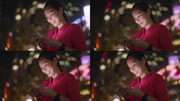 在城市夜晚使用智能手机的亚洲女性