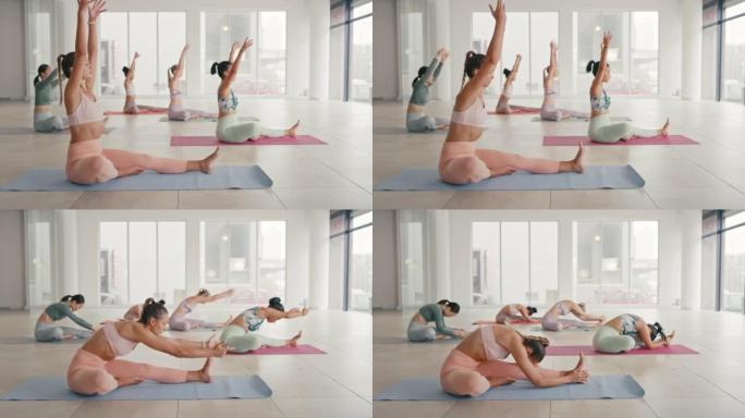 年轻女性在瑜伽课上伸展，在宽敞的健康中心做头到膝盖向前弯曲。健康的女性坐在一起在运动垫上做冥想和柔韧