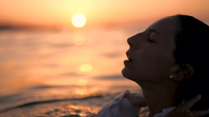 一位年轻快乐微笑的黑发女游客的真实特写镜头在日落暑假期间与近海游艇一起在海水中游泳。