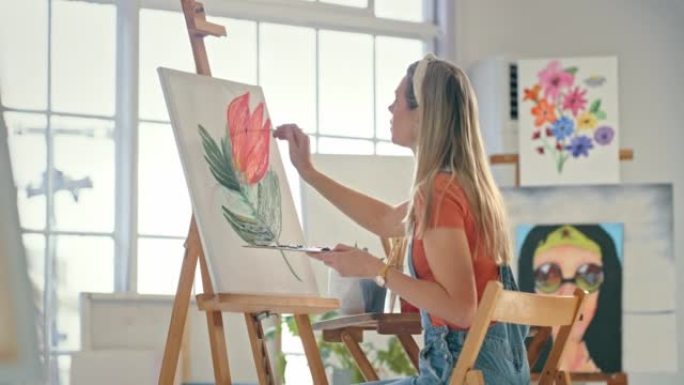 一位年轻的女画家在工作室里在画布上画彩画。严肃的女人在车间用画笔画一朵花。女人在她的美术馆里画一朵玫
