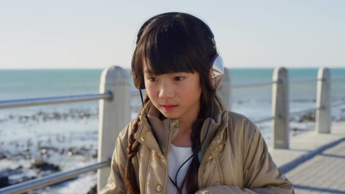 旅行，小女孩和耳机音乐在海滩长廊思考在日本度假。可爱的亚洲儿童流媒体音频应用程序在海洋深思熟虑，思考