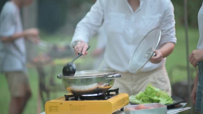 亚洲华人家庭妈妈搅拌面条炖汤烹饪在露营帐篷准备晚餐