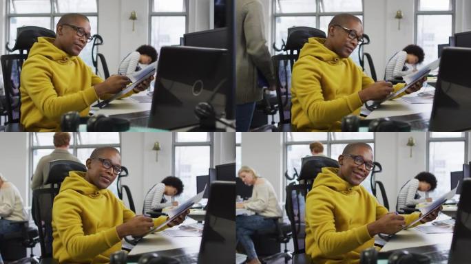 微笑的非洲裔美国创意商人的肖像坐在现代办公室的办公桌旁