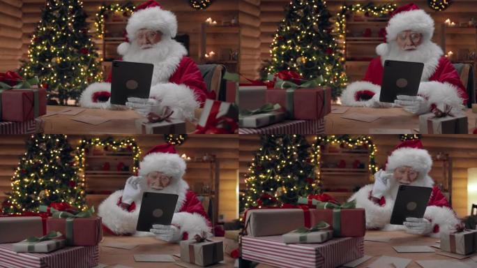 圣诞老人正在他的数字平板电脑上完成视频聊天，他说再见，并在屏幕上挥手，坐在他的办公室里