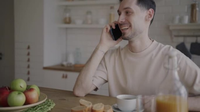早餐时坐在餐桌上的男人在手机上说话的肖像，厨房里的食物微笑着