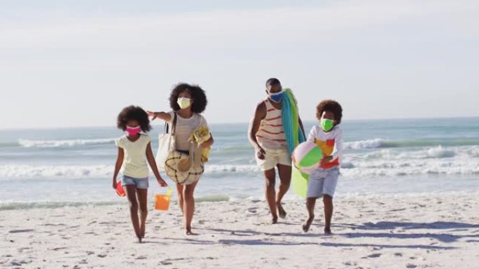 非裔美国父母和他们的孩子戴着口罩在海滩上携带沙滩设备