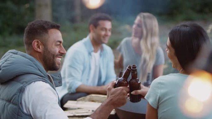 一群朋友露营坐在火旁做饭，一起喝啤酒