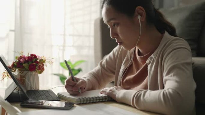 亚洲妇女戴着耳机，与老师一起学习，在笔记本电脑屏幕上进行在线家庭学习