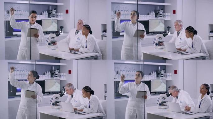 医学研究实验室的科学家团队讨论了疫苗的化学式。女研究员在玻璃墙上与同事在现代实验室的桌子上工作