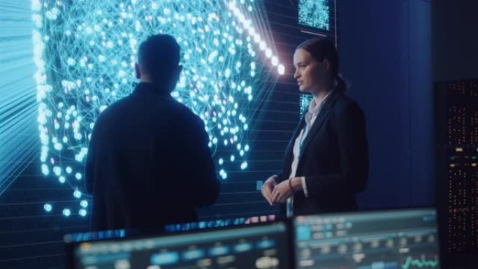 项目经理和计算机科学工程师在使用大屏幕显示神经连接和数据时交谈。电信公司系统控制和监控室。