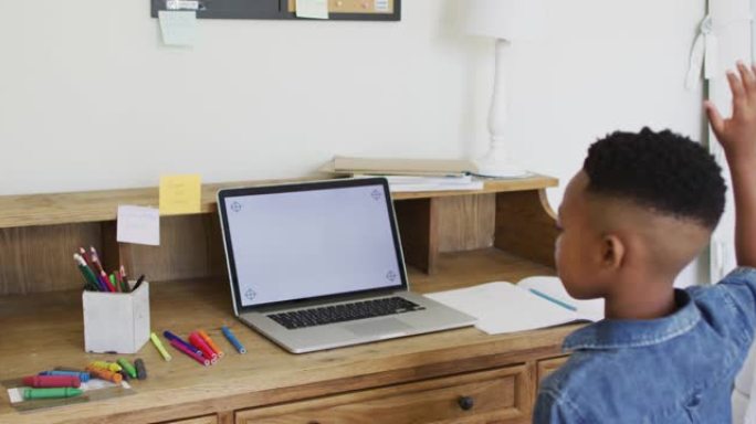 在网上学校上课的非裔美国男孩在家中使用屏幕上的笔记本电脑复制空间举手