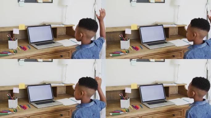 在网上学校上课的非裔美国男孩在家中使用屏幕上的笔记本电脑复制空间举手