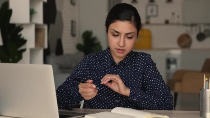 在笔记本电脑上工作的印度妇女在抄写本上做笔记