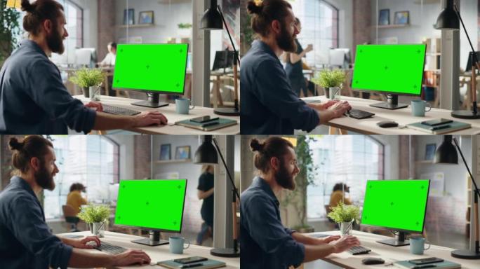 时尚的长发胡须专家坐在创意机构的办公桌前。年轻时尚的男人在绿屏模拟显示器的台式电脑上工作。办公室团队