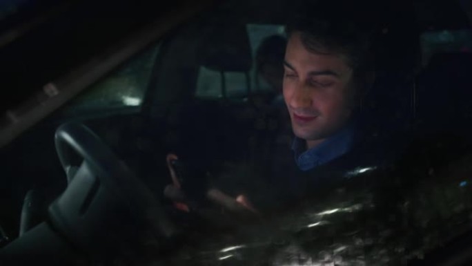一位年轻英俊的商人正在夜间在城市中心的现代汽车中使用智能手机，而外面正在下雨。