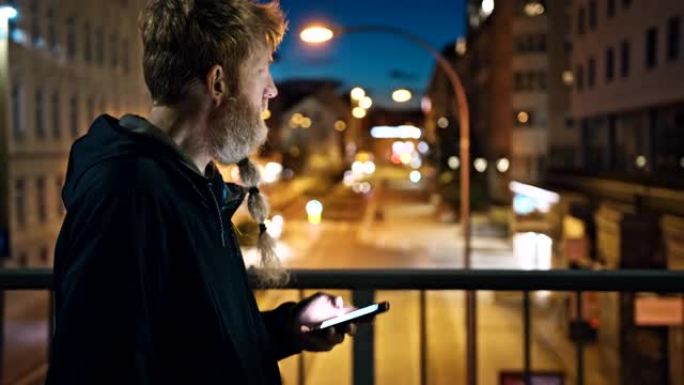 晚上在城市的人行道上行走时，留着长胡须的男子使用智能手机