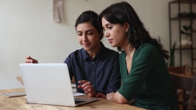 两名多种族女性同事盯着笔记本电脑屏幕聊天