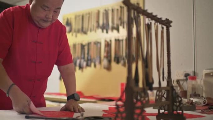 亚洲中国男性为即将到来的农历新年庆祝活动而练习中国书法，目的是通过将其写在红色纸上来实现繁荣和良好的