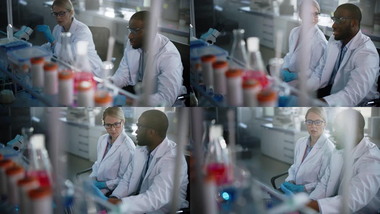 光明医学实验室与不同的研究科学家团队合作。微生物学家在显微镜下用笔记本电脑与生物化学家交谈。高科技设