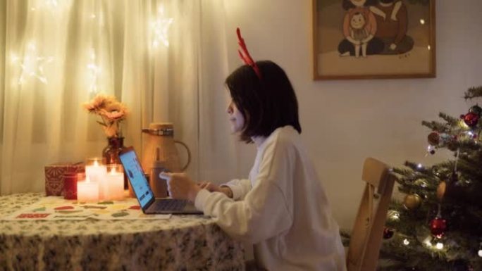 微笑的亚洲女性拿着笔记本电脑坐在家里买圣诞礼物。