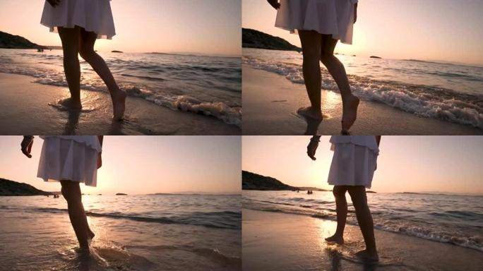 一个穿着白色太阳裙的年轻无忧无虑的女人在日落度假旅行期间沿着海滨沙滩散步的真实特写镜头。